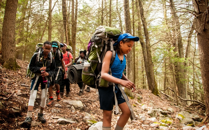 A group of young people wearing backpacks high through a wooded area 